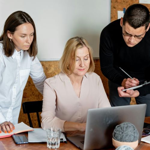 Three colleagues in an office collaborate around one laptop